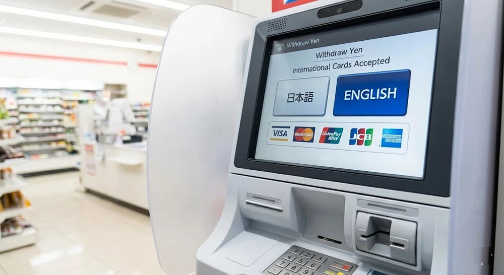 A close-up photograph of an ATM screen inside a Japanese convenience store. The screen displays "Withdraw Yen" and "International Cards Accepted", with a large button to select "ENGLISH" language. Below the buttons are logos for Visa, Mastercard, UnionPay, JCB, and American Express.