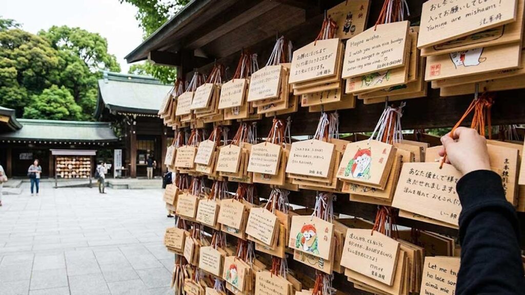 Wooden Ema plaques (wishing plates) hanging at a Japanese Shinto shrine, with a visitor hanging up their handwritten wish